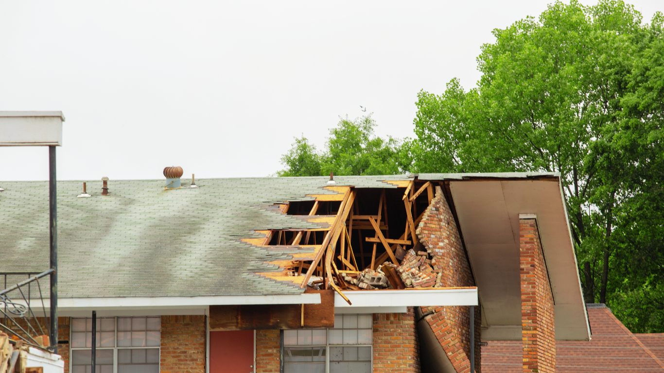 Damaged roof of a brick building with exposed wood and collapsed sections, highlighting the urgent need for storm damage restoration.